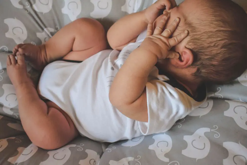 Bebê escondendo o rosto, chorando. Importante ficar atento aso sinais de pega incorreta na amamentação.
