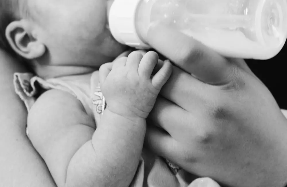 imagem em preto e branco de bebê tomando leite na mamadeira, para ilustrar post sobre como tirar o leite materno.