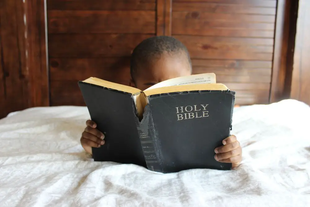 Imagem de um menino lendo a bíblia. Imagem para representar as ideias de frases para chá de bebê com temas evangélicos ou religiosos