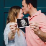 foto de casal, homem beijando a testa da mulher, com foto de ultrassom de bebê. Foto para capa do post sobre frases de gravidez para status.