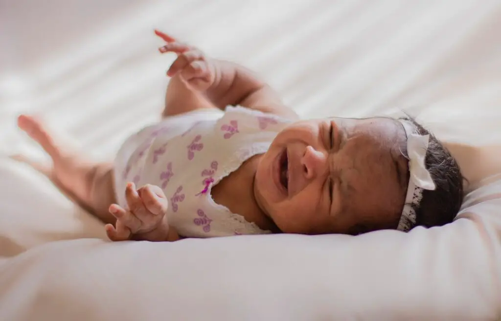 bebe chorando, em cima de um colchão para ilustrar os impactos dos saltos de desenvolvimento no humor do bebê