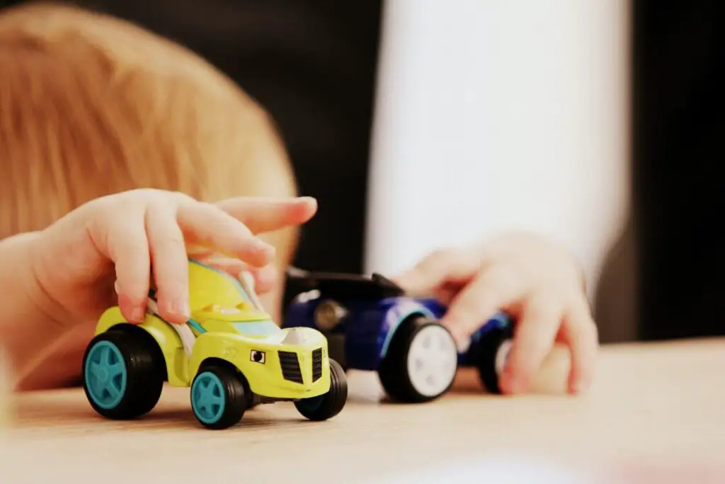 cabeça desfocada de menino loiro,  brincando com dois carrinhos, um amarelo e outro azul para ilutrar a função do brinquedo para Vygotsky