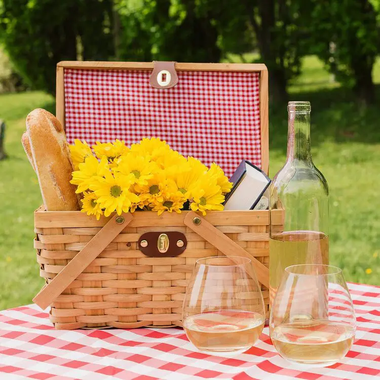 cesta de piquenique infantil elegante, com pães, flores e livros dentro. Uma garrafa de bebida e duas taças