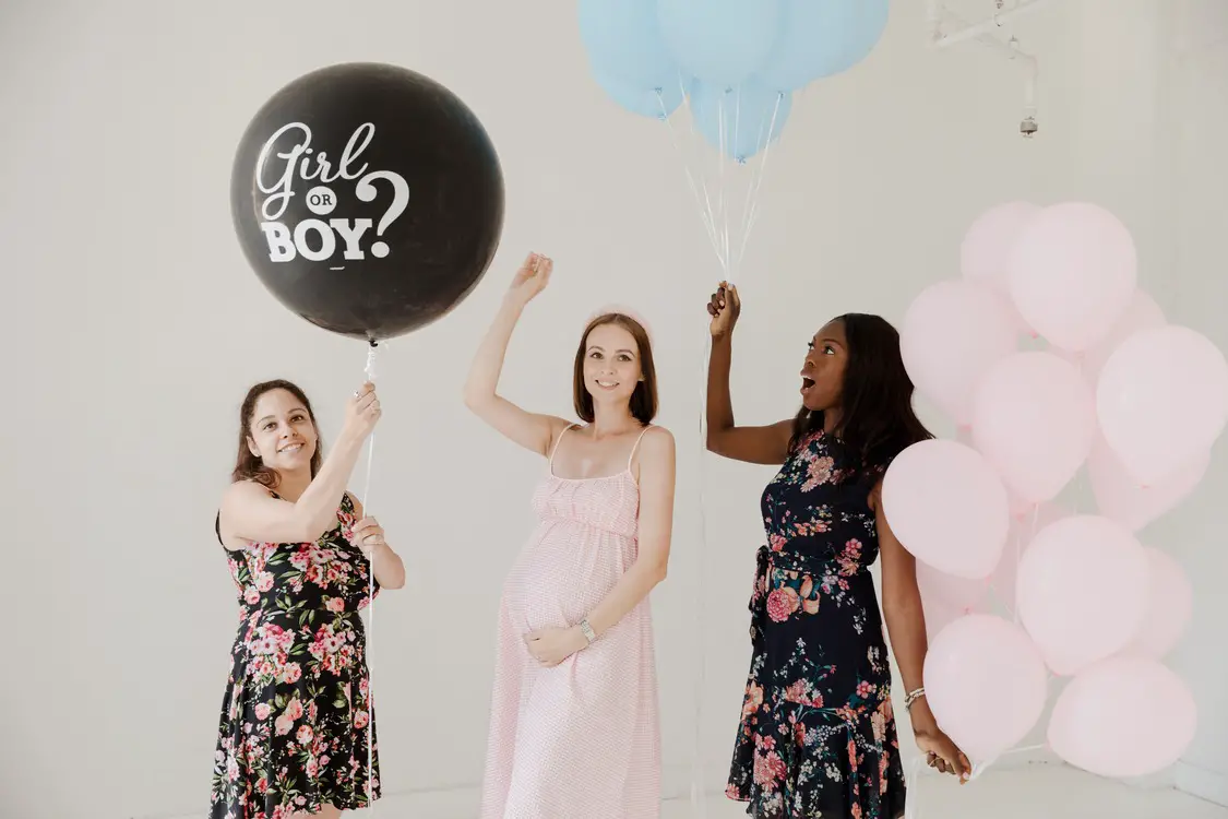 tres mulheres, sendo que a do meio está grávida segurando um balão escrito "boy or girl" em uma festa de chá revelação simples