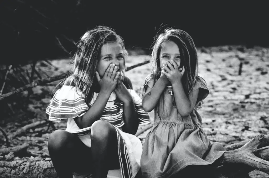 duas meninas loiras, em foto preto e branco, as duas estão dando risada, cobrindo a boca. para ilustrar o post sobre nomes femininos diferentes.