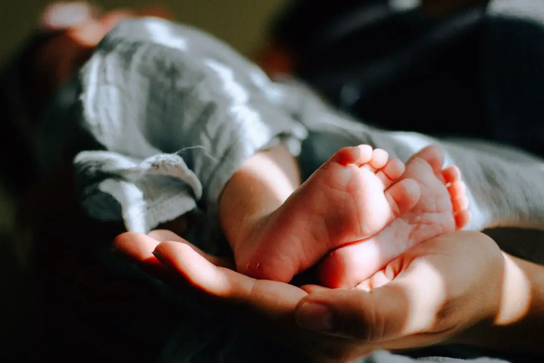 imagem dois pezinhos de bebê, em cima de uma mão para o post sobre visitar recém nascido.