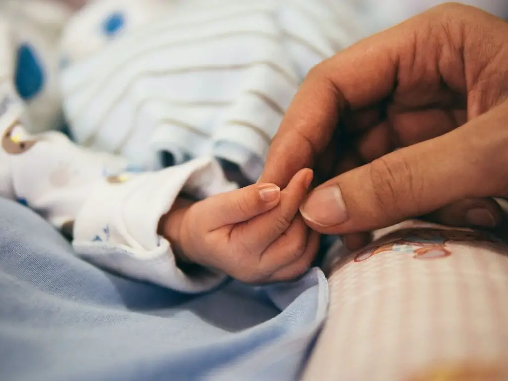 imagem de mãozinha pequena de bebê recém nascido, e uma outra mão adulta segurando, para post visitar recém-nascido