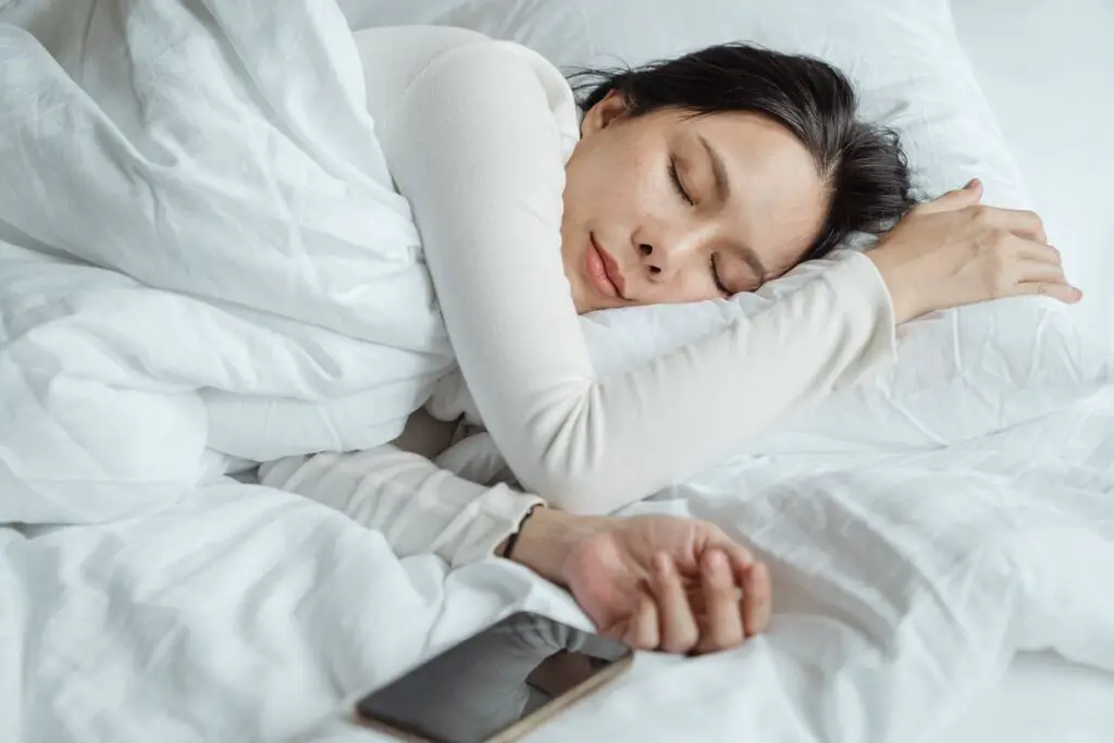 mulher dormindo em uma cama branca, com um celular deixado de lado na cama. Sonhar com gravidez.