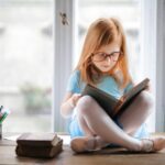 menina ruiva de óculos, lendo um livro de histórias de princesas curtas