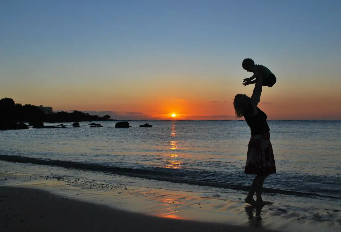 mãe segurando bebe no alto, em uma praia, no por do sol, mensagem para mãe de primeira viagem