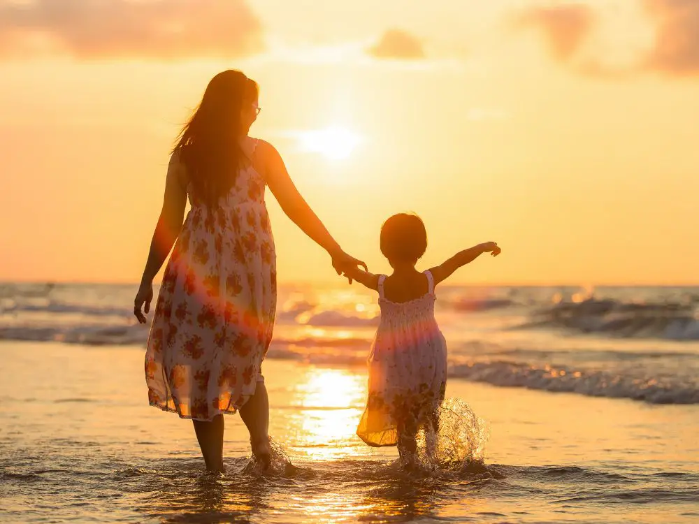 mãe e filha andando na praia, de costas, sol se pondo, mensagens de dia das mães emocionantes