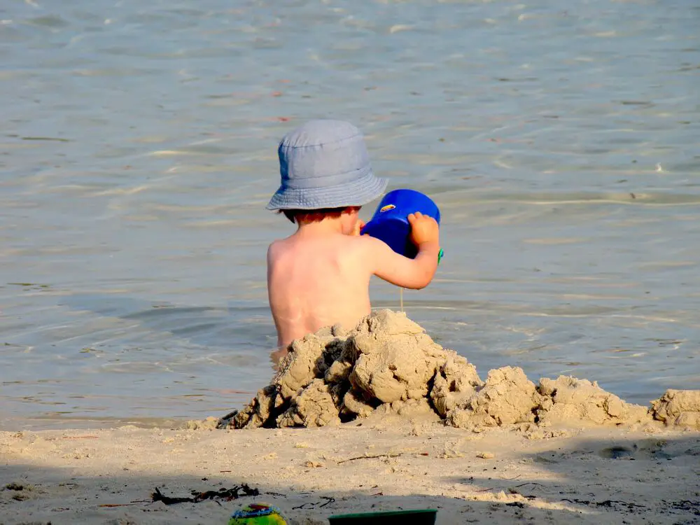 Image of a boy with his back turned, wearing a blue hat, amidst sand, in front of the sea. To illustrate the text about Greek boy names.