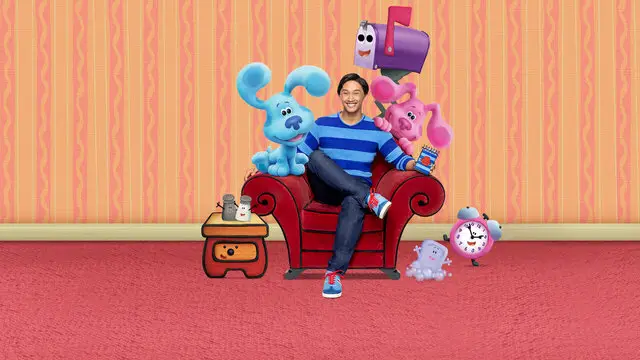 Desenhos Educativos e de baixo estímulo na Netflix: um homem sentado em um sofá marrom, e três personagens animados ao redor dele, um cachorro azul, um cachorro rosa, uma caixa de correio, e um ser cinza no chão com cor rosa e paredes com papel de parede rosa e laranja claro.