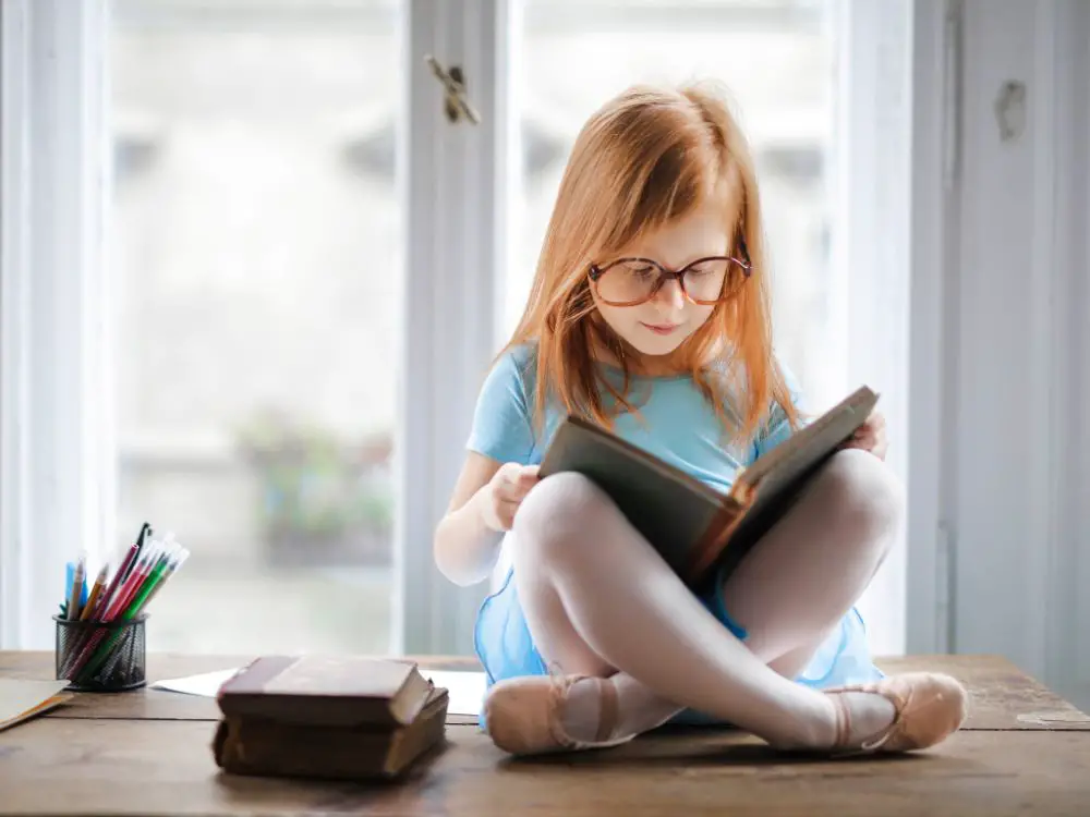 Red-haired girl wearing glasses, reading a book of short princess stories for kids.