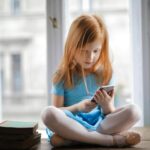menina ruiva mexendo em um celular, para ilustrar post sobre Tempo de tela por idade