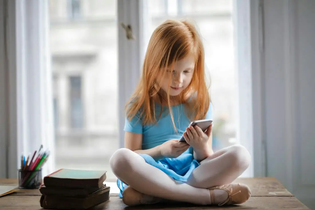 menina ruiva mexendo em um celular, para ilustrar post sobre Tempo de tela por idade